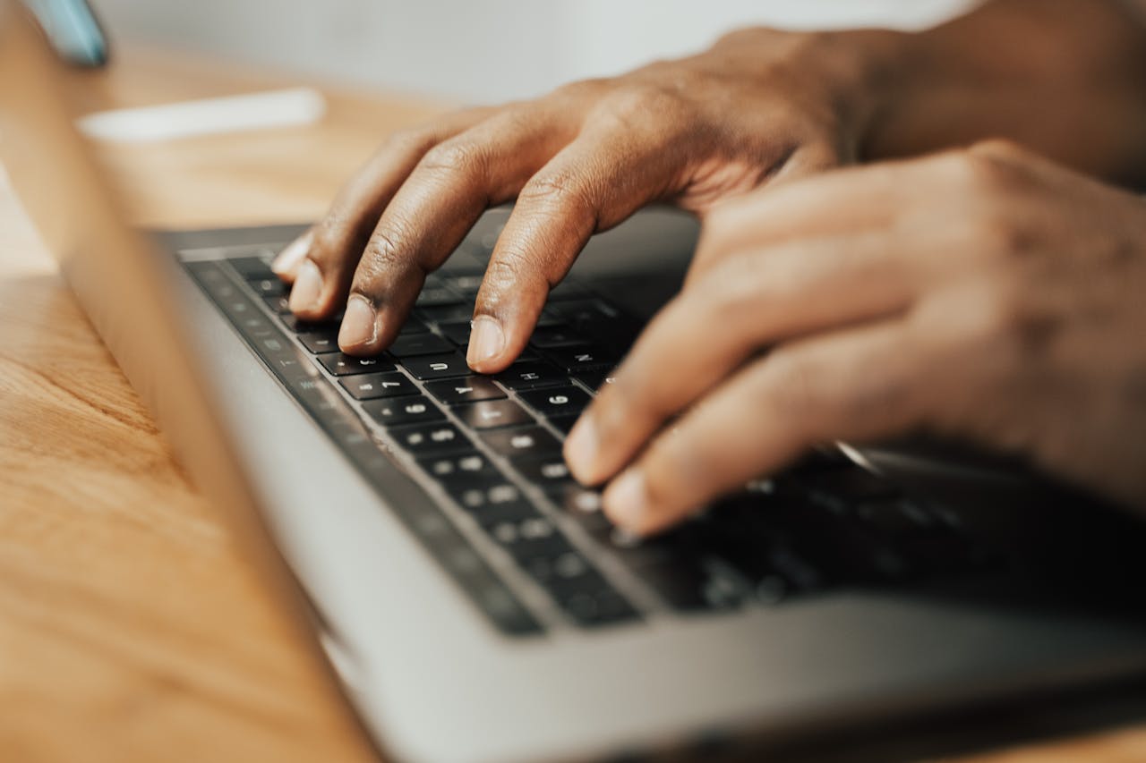 Focused shot of hands typing on a laptop keyboard on a wooden table, illustrating remote work.